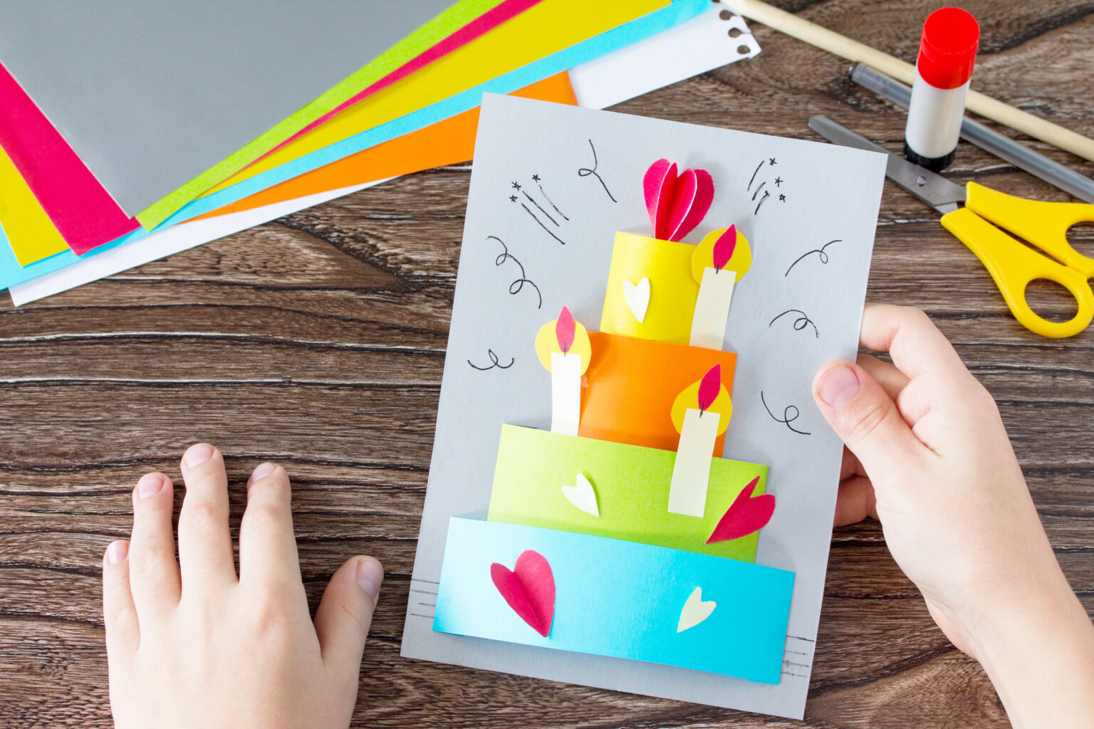 A child’s hands holding a birthday card with a cake made of paper on it